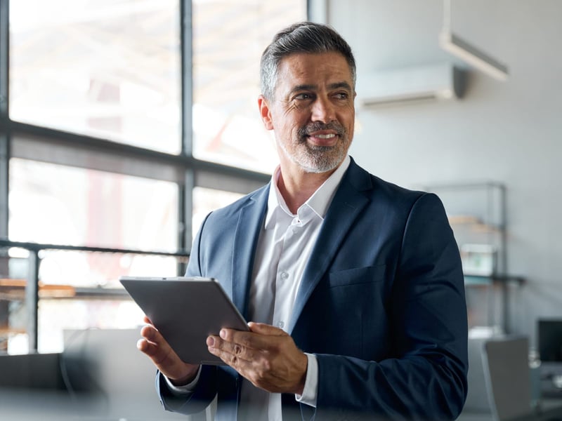 Happy business executive standing in office using tablet